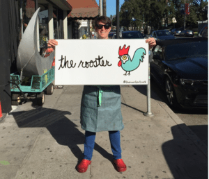 Chef Rouha Sadighi holding The Rooster sign
